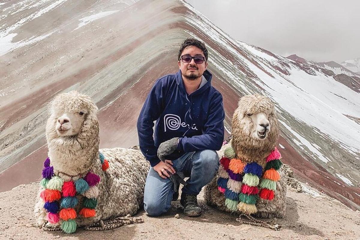 a man kneeling next to two sheep dressed in yarn