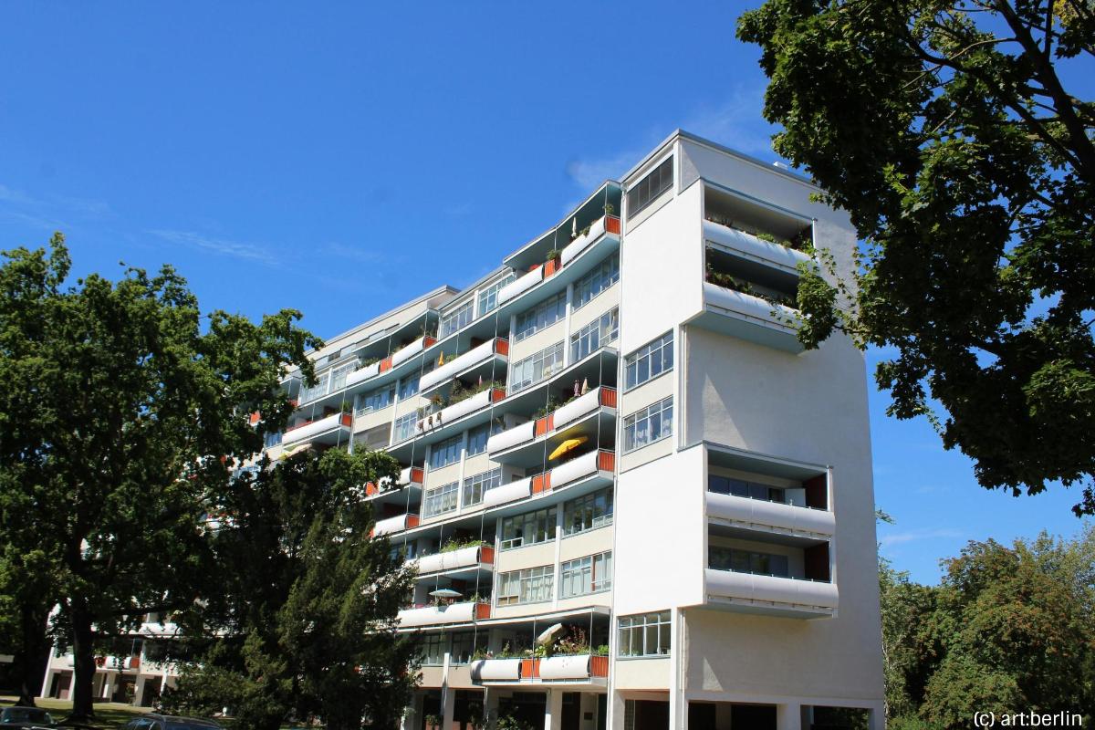 een wit appartementengebouw met bomen ervoor