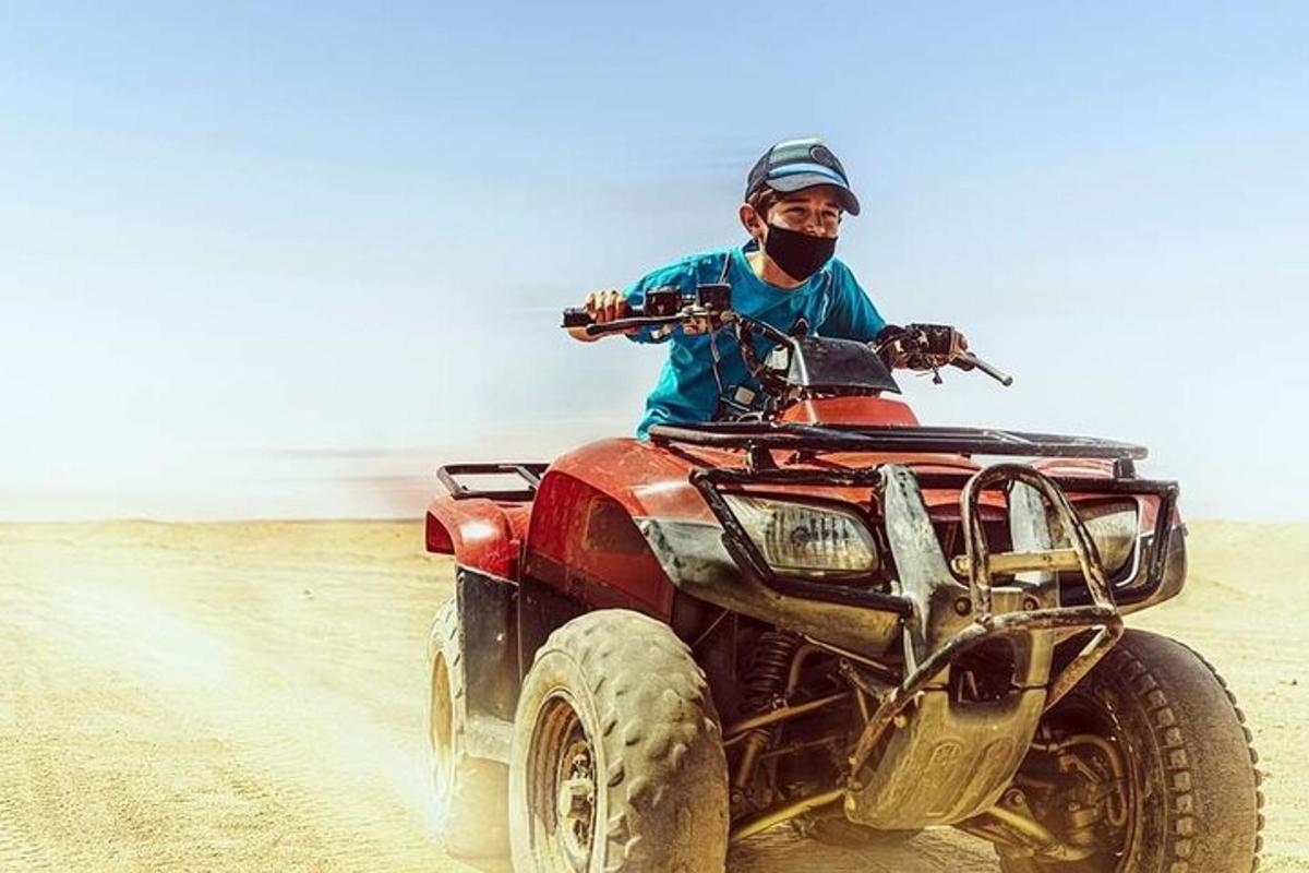Un hombre conduciendo un vehículo todo terreno rojo en el desierto.