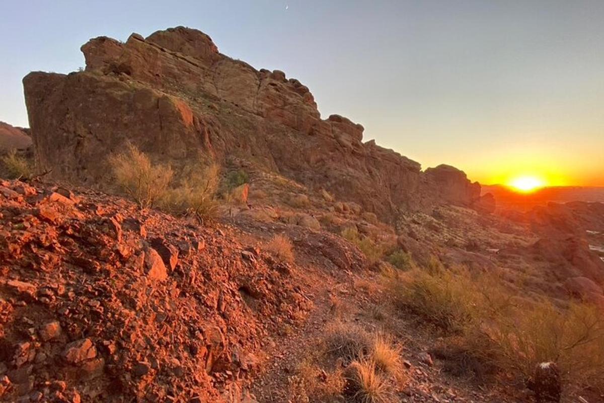 Una puesta de sol sobre una montaña rocosa con la puesta del sol