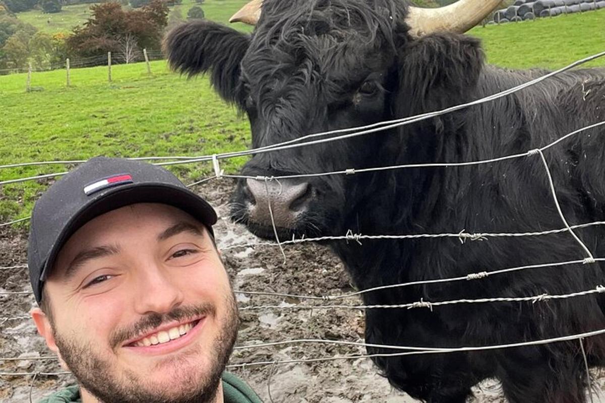mężczyzna stojący przed płotem obok krowy
