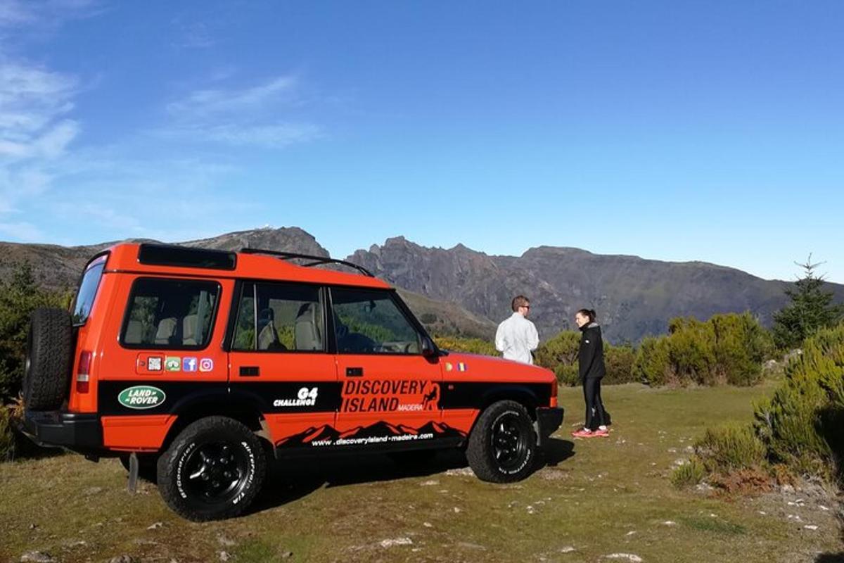 một chiếc xe jeep màu đỏ đậu trên cánh đồng với hai người đàn ông