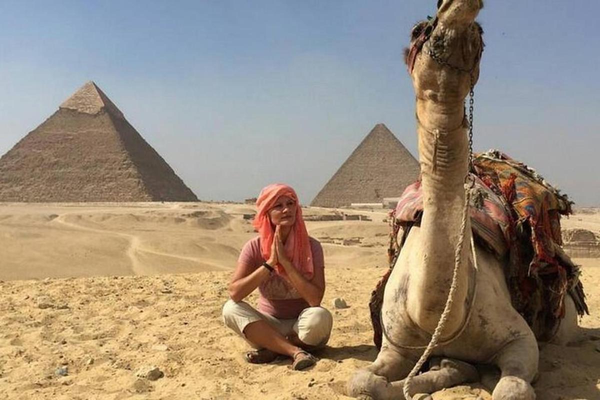 en kvinne som sitter ved siden av en kamel foran pyramider