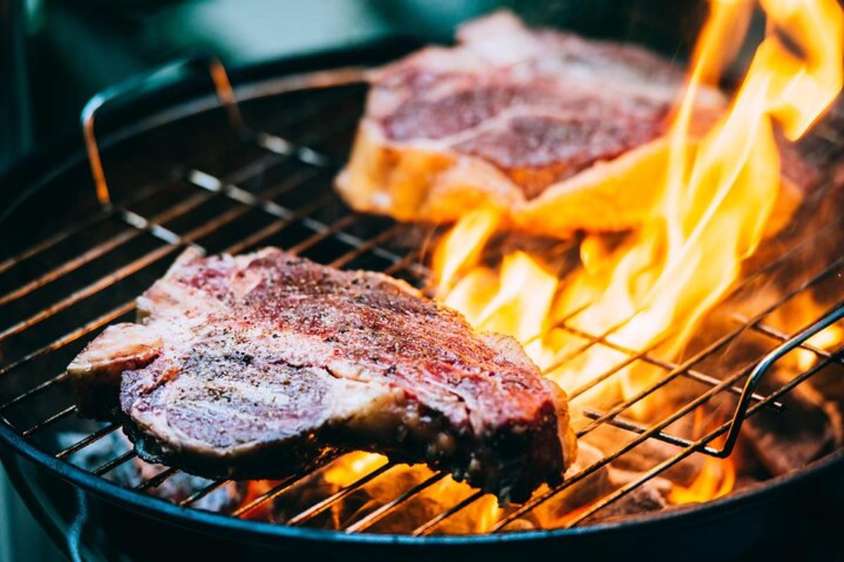 Dos piezas de carne cocinándose en una parrilla con llamas