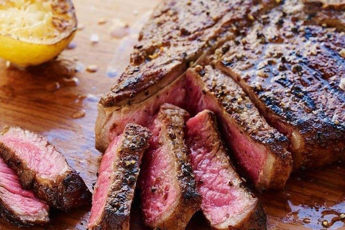 Un trozo de pan con carne y un limón sobre una mesa.