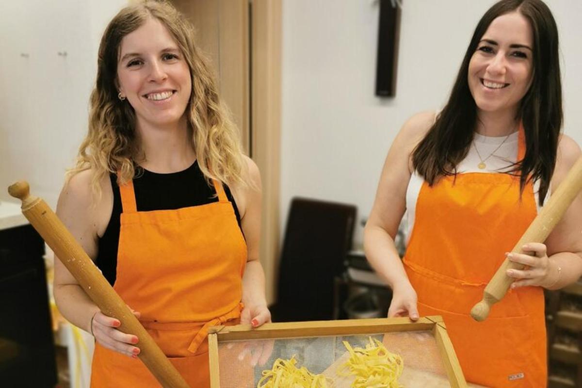 két narancssárga kötényt viselő nő egy képet és egy festményt tart a kezében