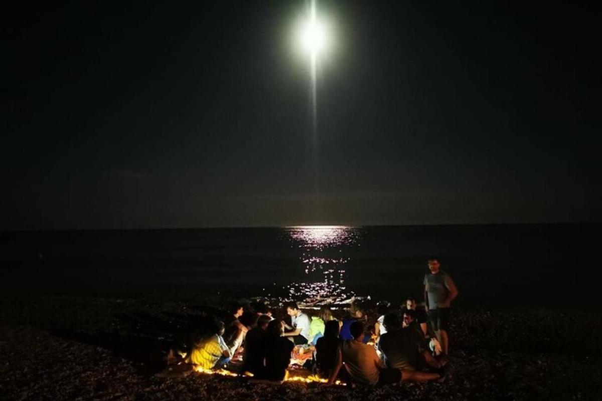 sekumpulan orang yang duduk di pantai pada waktu malam