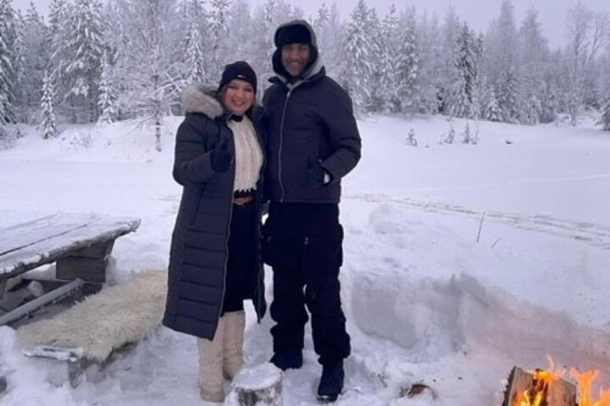 a man and woman standing next to a fire in the snow