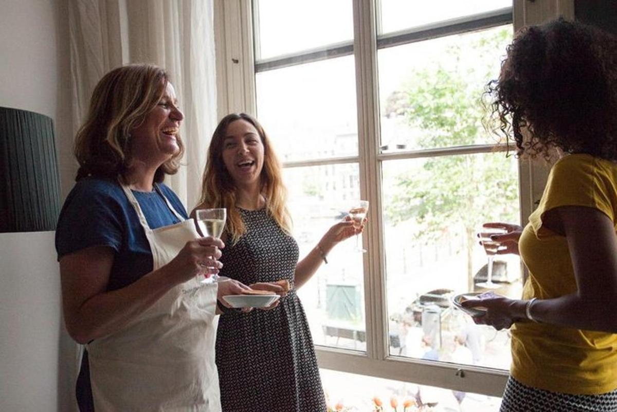 three women laughing and drinking wine in front of a window