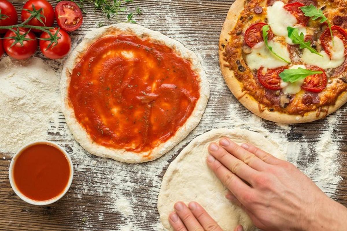 Dvě pizzy sedící na dřevěném stole s osobou, která pizzu připravuje