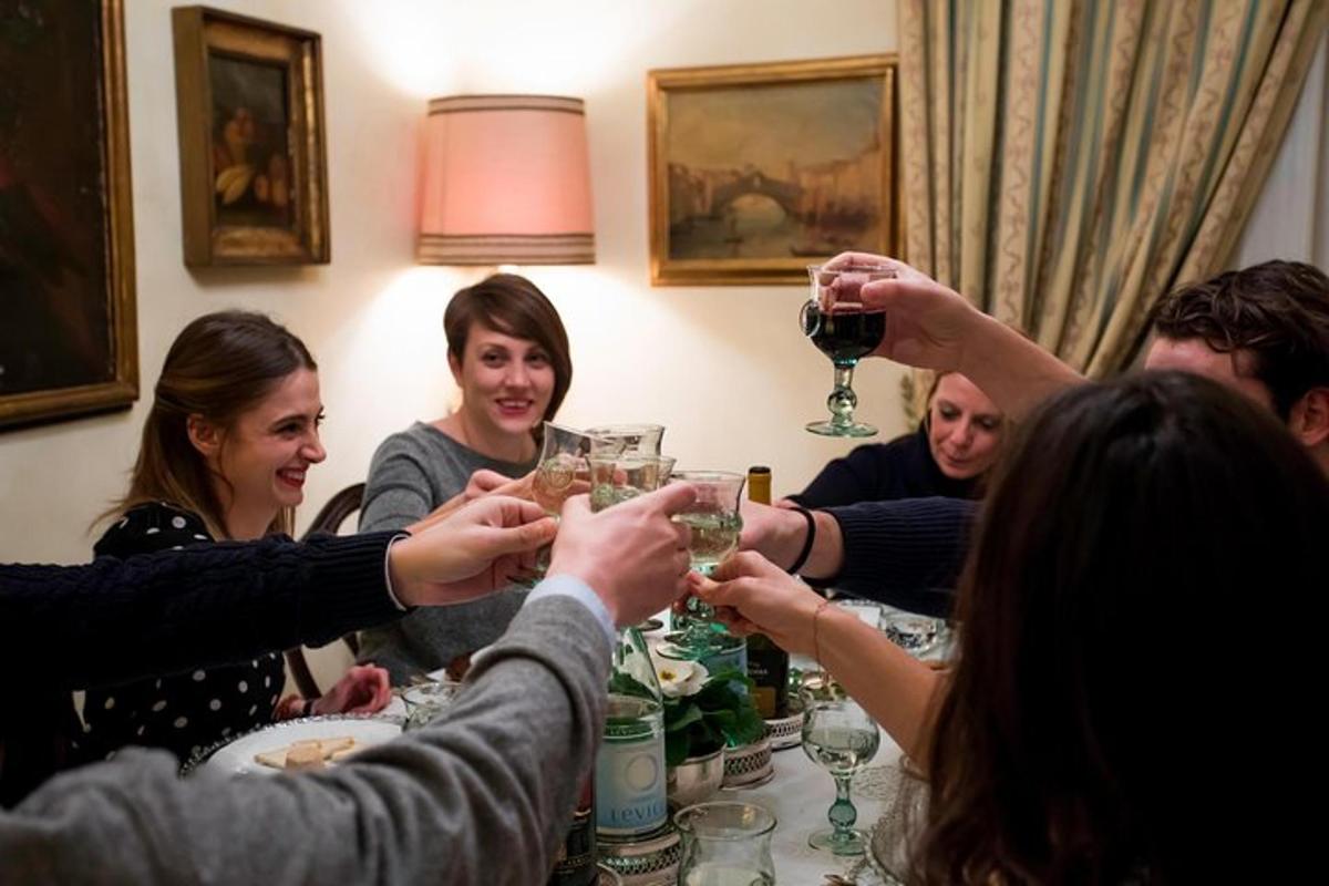 cilvēku grupa, kas sēž ap galdu un dzer vīnu