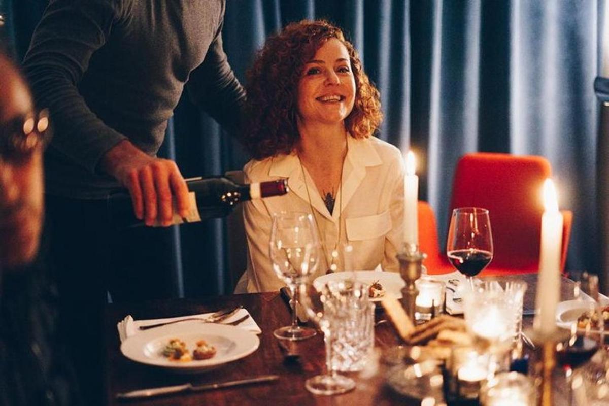 a woman is sitting at a table pouring a glass of wine