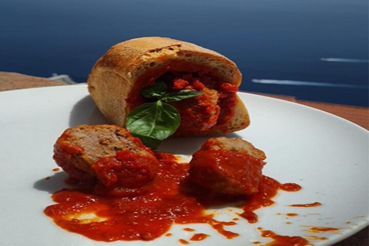 a white plate with a sandwich with meatballs and sauce