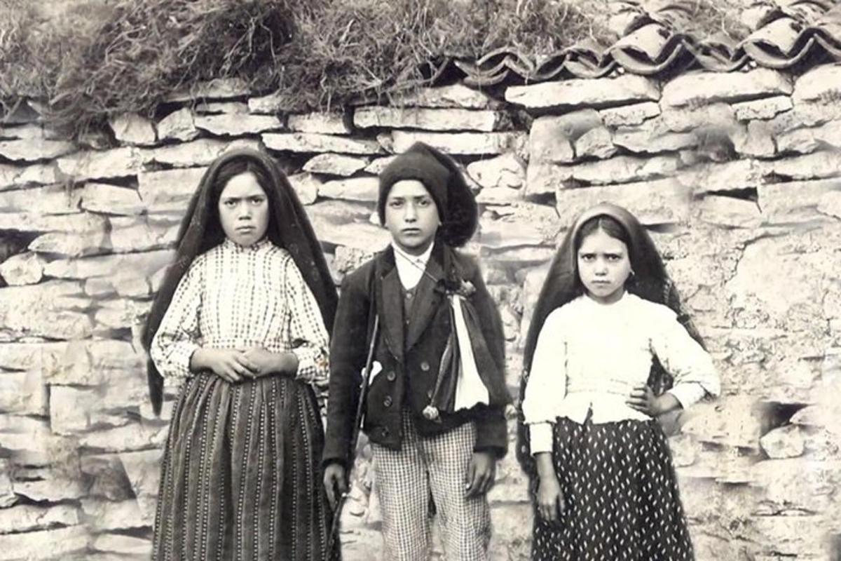 uma foto em preto e branco de três meninas em frente a um muro de pedra