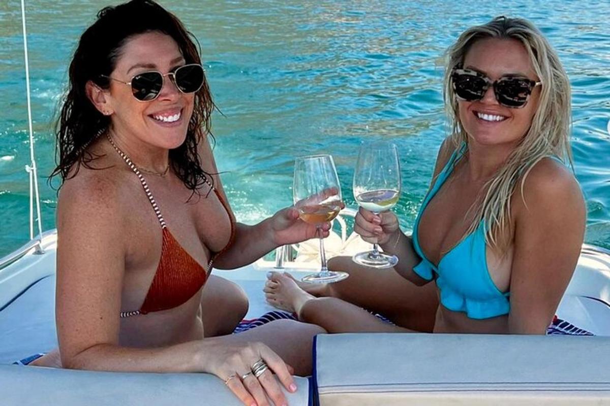 Δύο γυναίκες με μαγιό κάθονται σε μια βάρκα με ποτήρια κρασιού