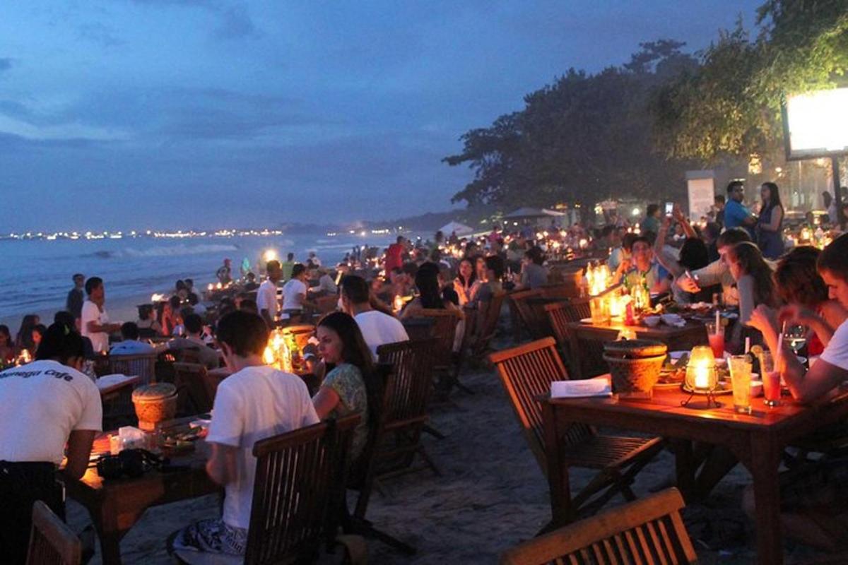 a crowd of people sitting at tables on the beach at night
