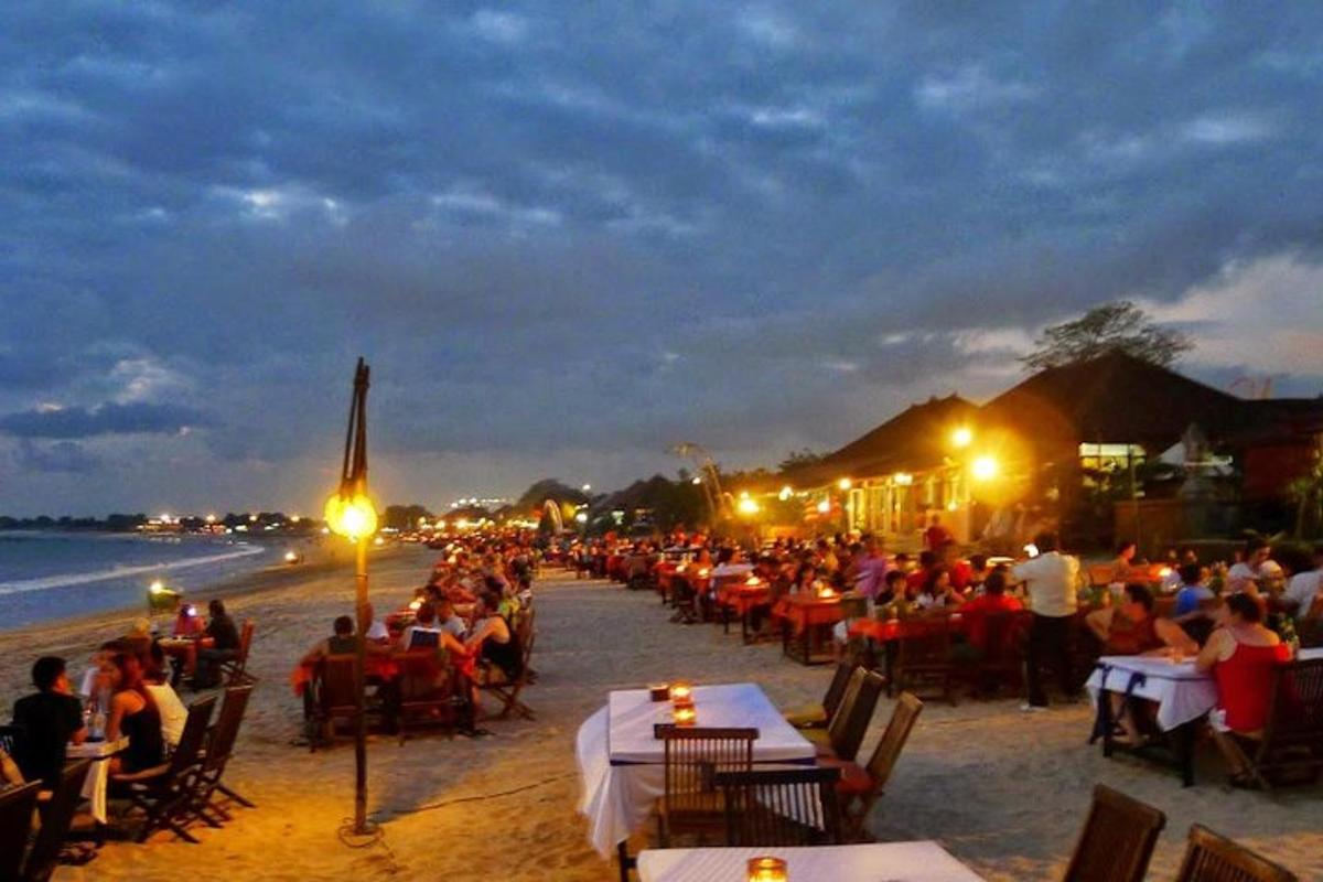 a group of people sitting at tables on the beach at night