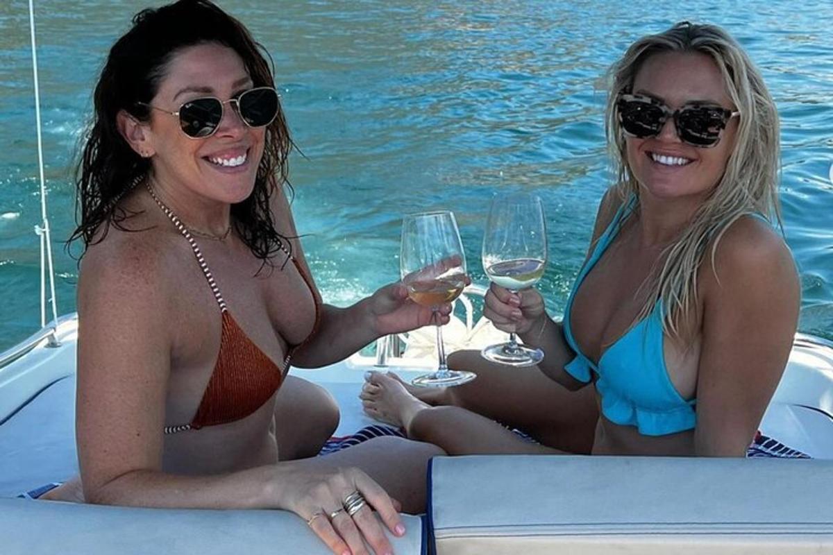 Δύο γυναίκες με μαγιό κάθονται σε μια βάρκα με ποτήρια κρασιού