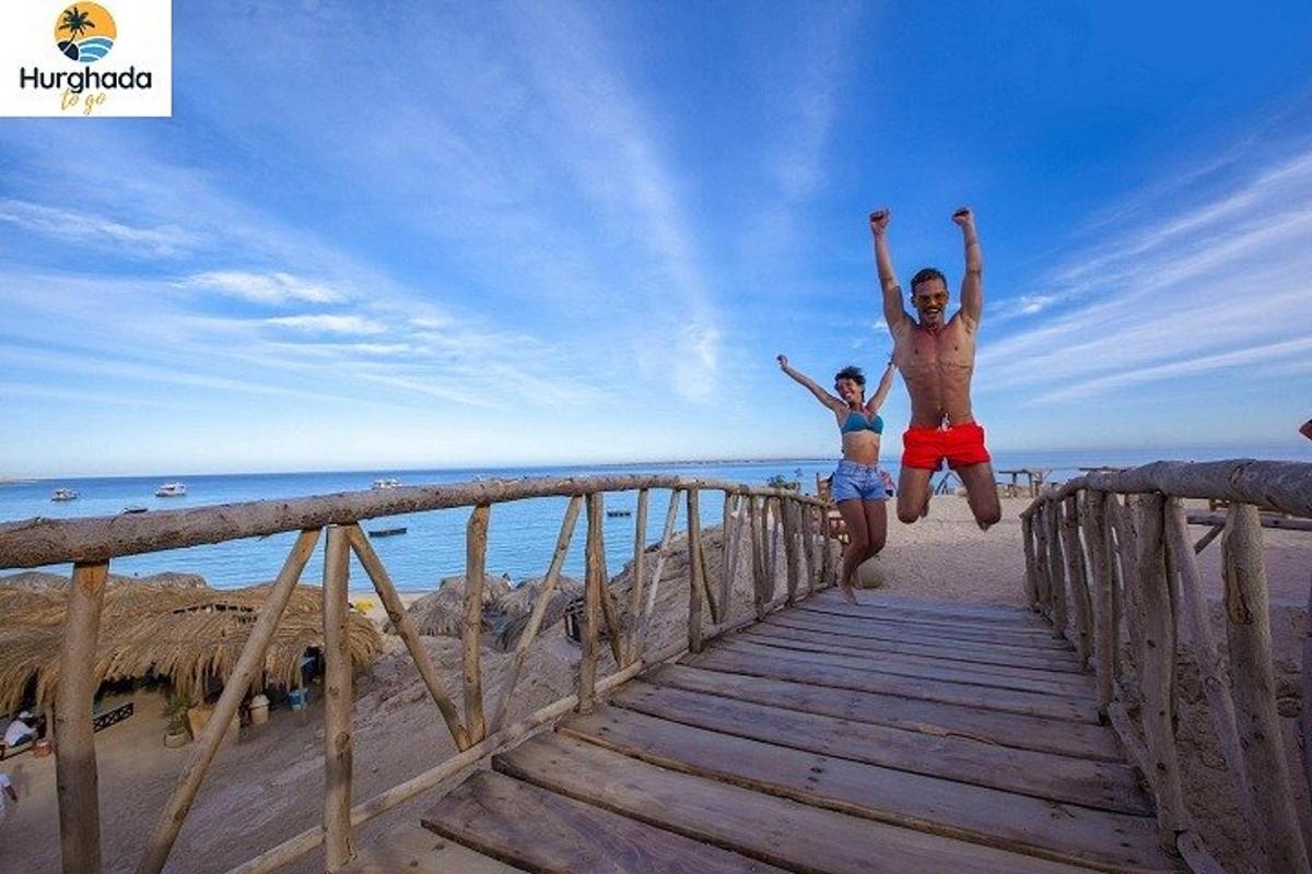 a man and woman jumping off a wooden bridge at the beach