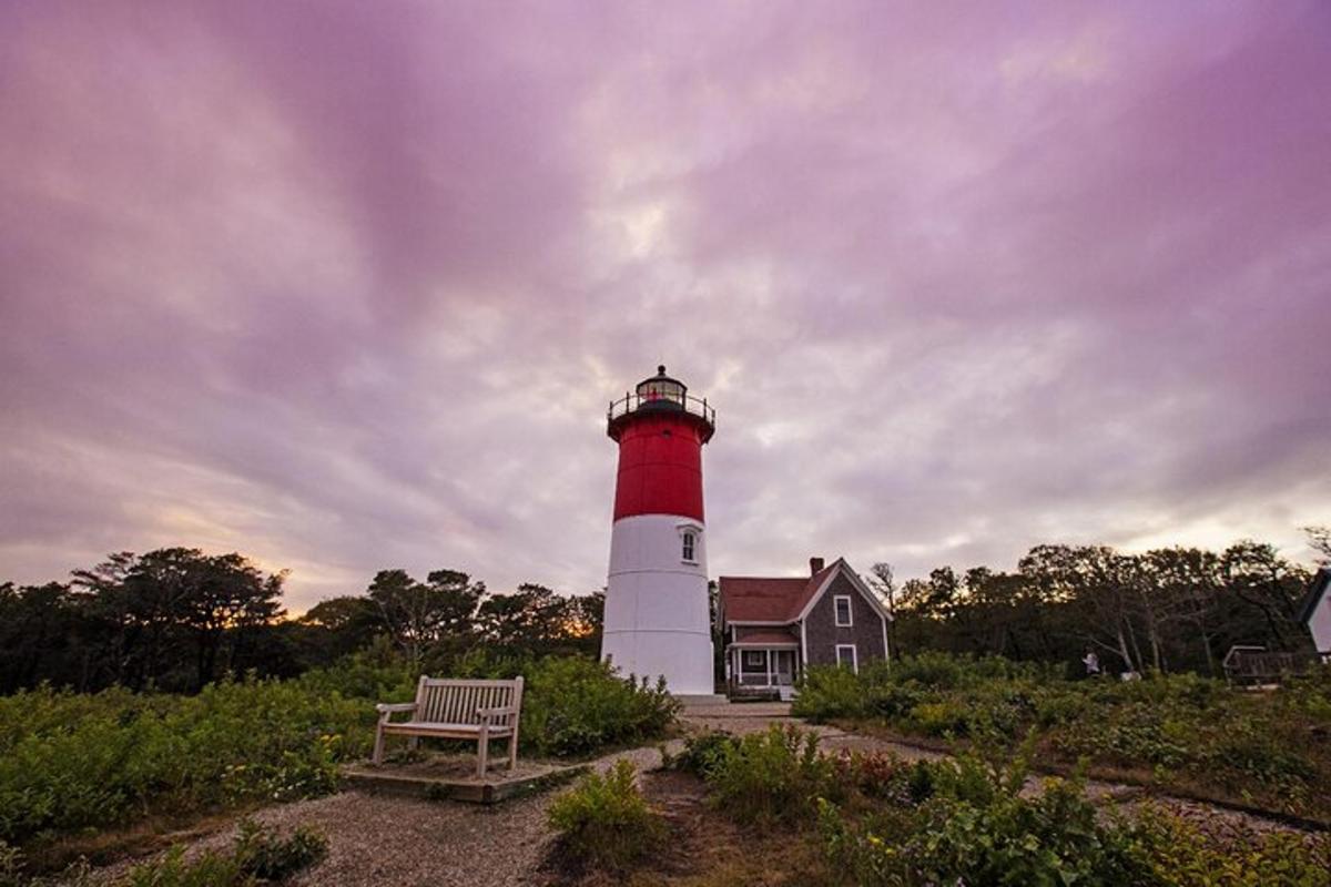 a red and white lighthouse with a bench in front of a house
