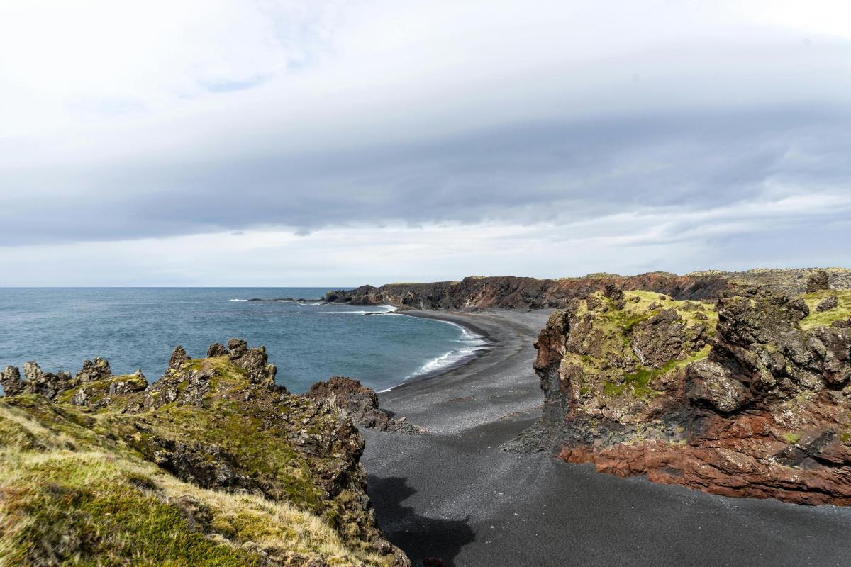 ein schwarzer Strand mit Felsen und dem Meer