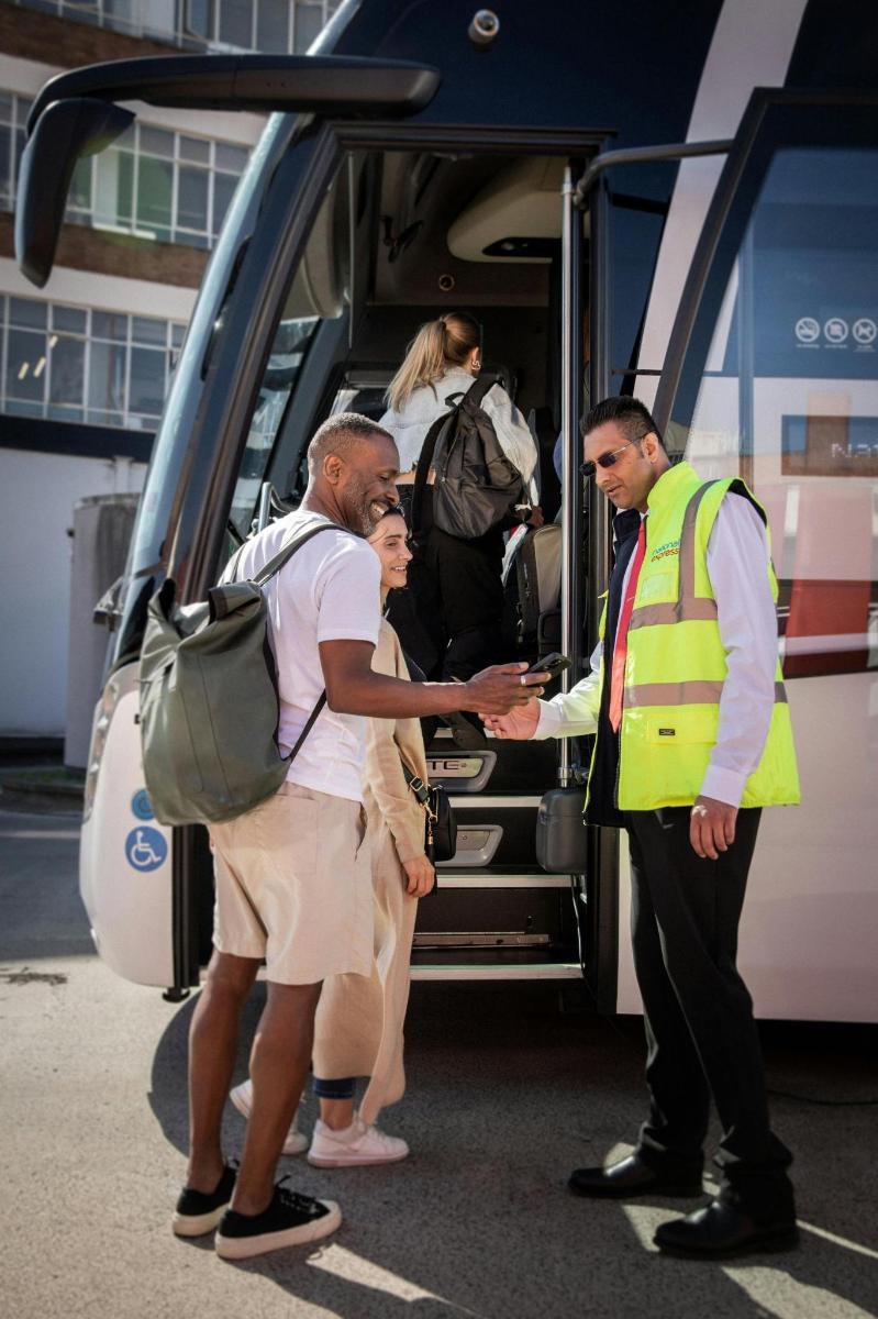 un bărbat în vestă galbenă dă mâna cu o persoană care coboară dintr-un autobuz