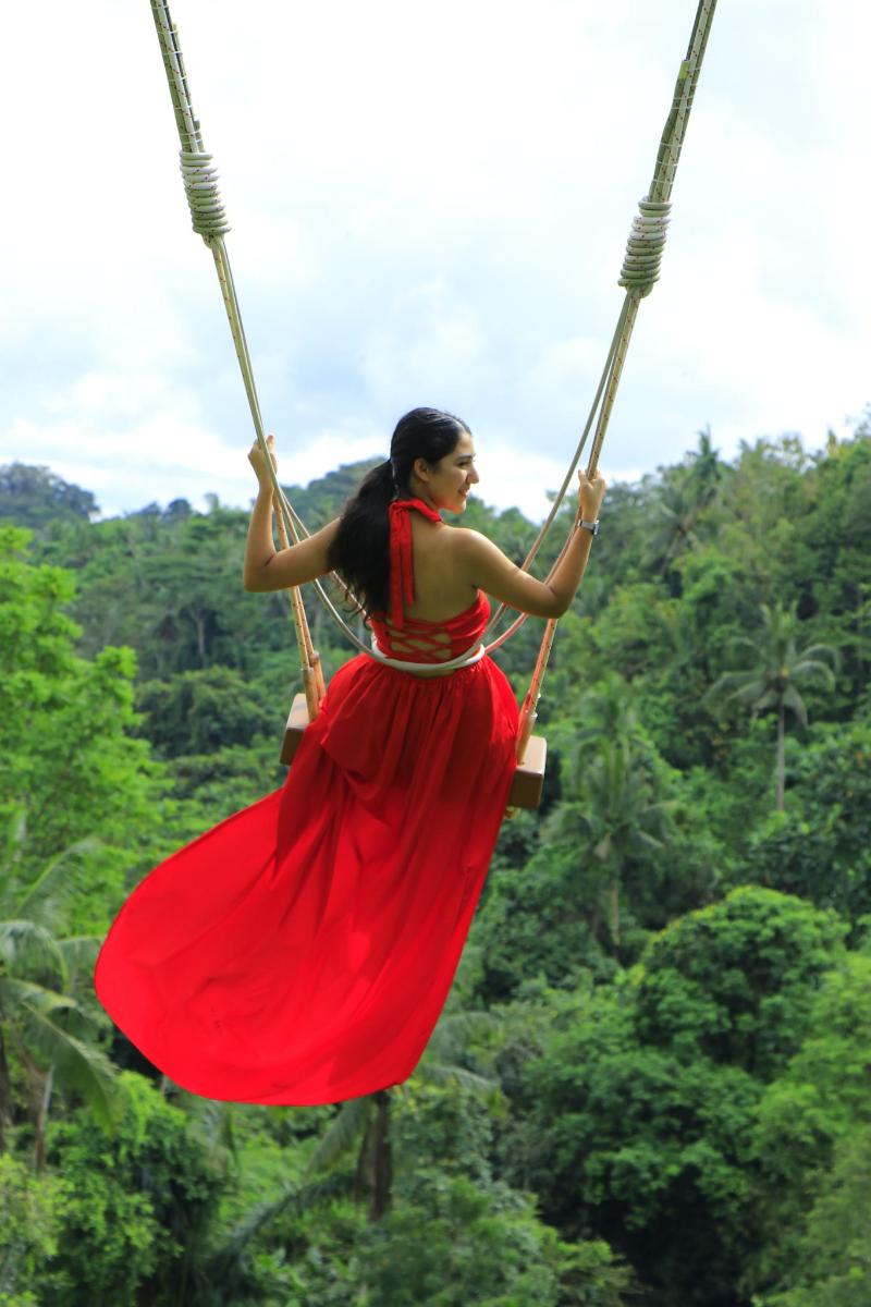 a woman in a red dress swinging on a rope swing