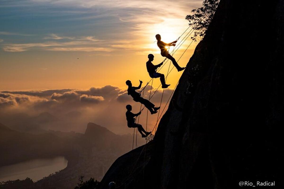 um grupo de pessoas escalando uma montanha ao pôr do sol