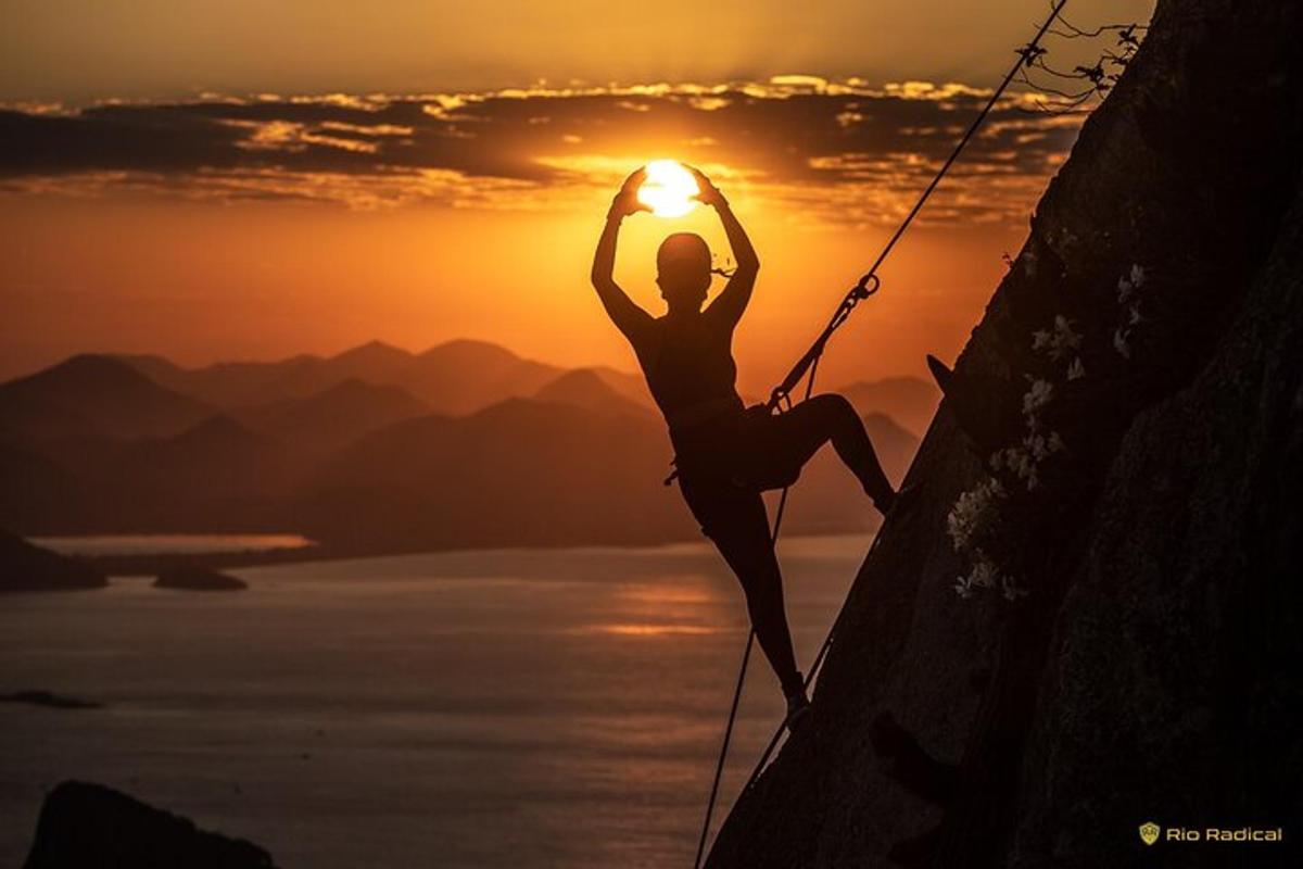 uma mulher está escalando uma parede de rocha ao pôr do sol