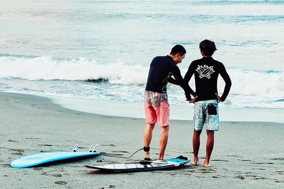two men standing next to a surfboard on the beach