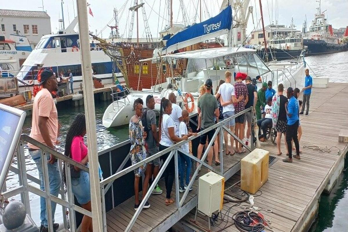 μια ομάδα ανθρώπων που στέκονται σε μια αποβάθρα δίπλα σε μια βάρκα