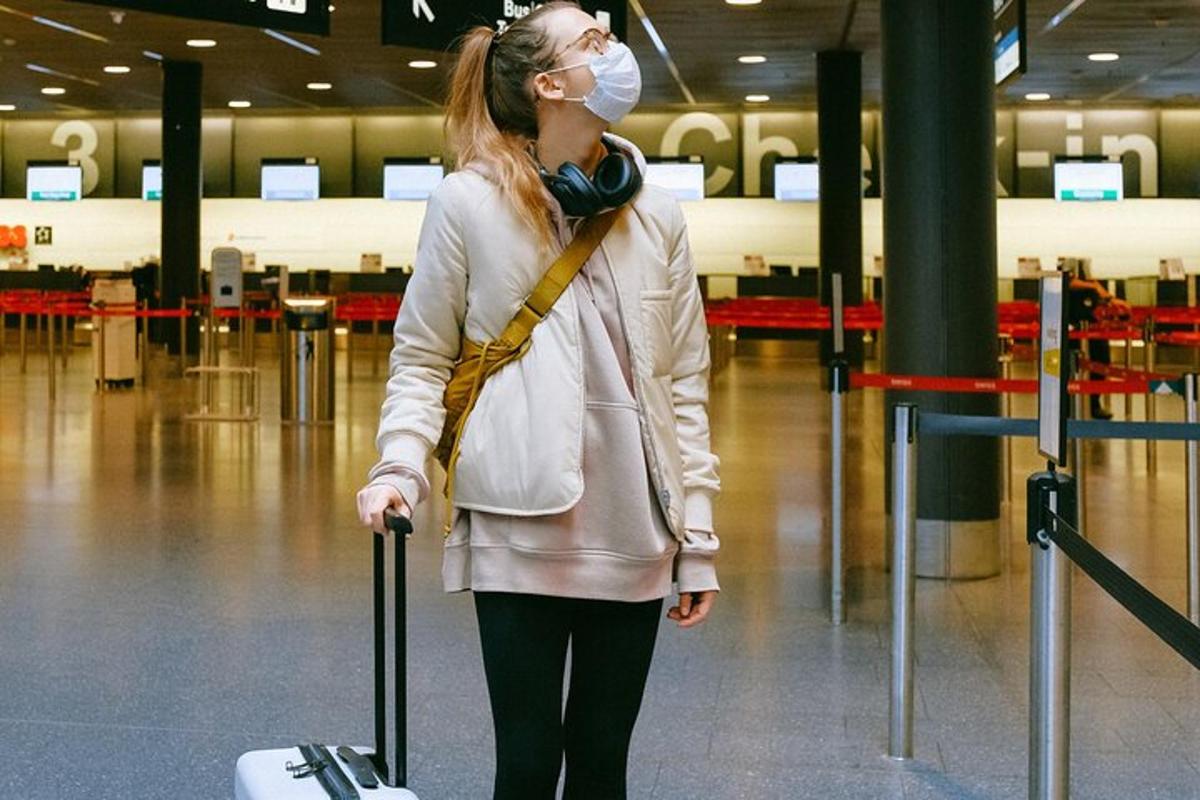 Una mujer con una máscara y tirando de una maleta en un aeropuerto.