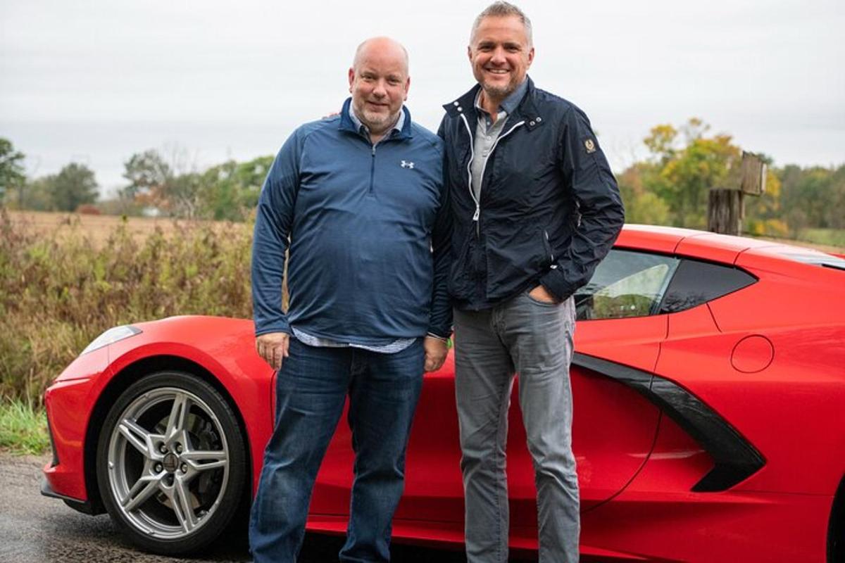 two men are standing next to a red car