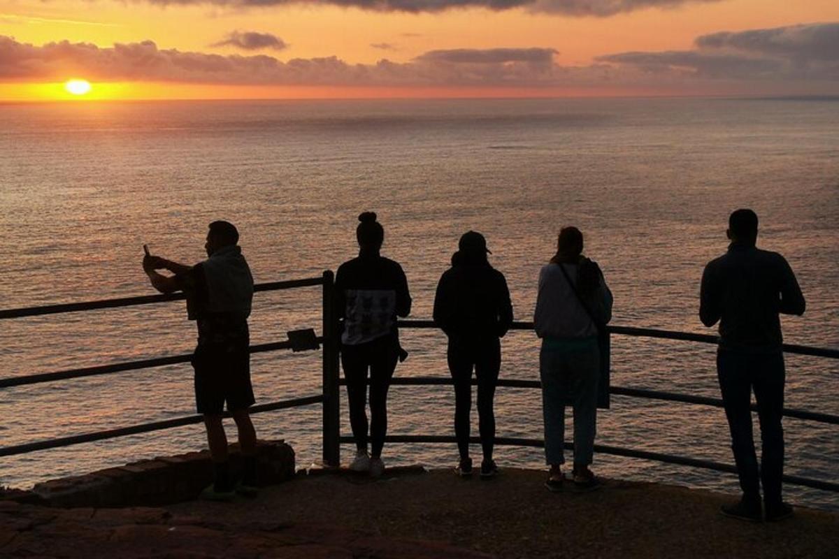 um grupo de pessoas em pé em um píer assistindo ao pôr do sol