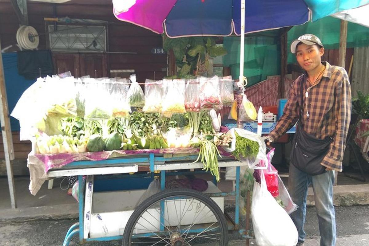 Un hombre de pie junto a un carrito con verduras.