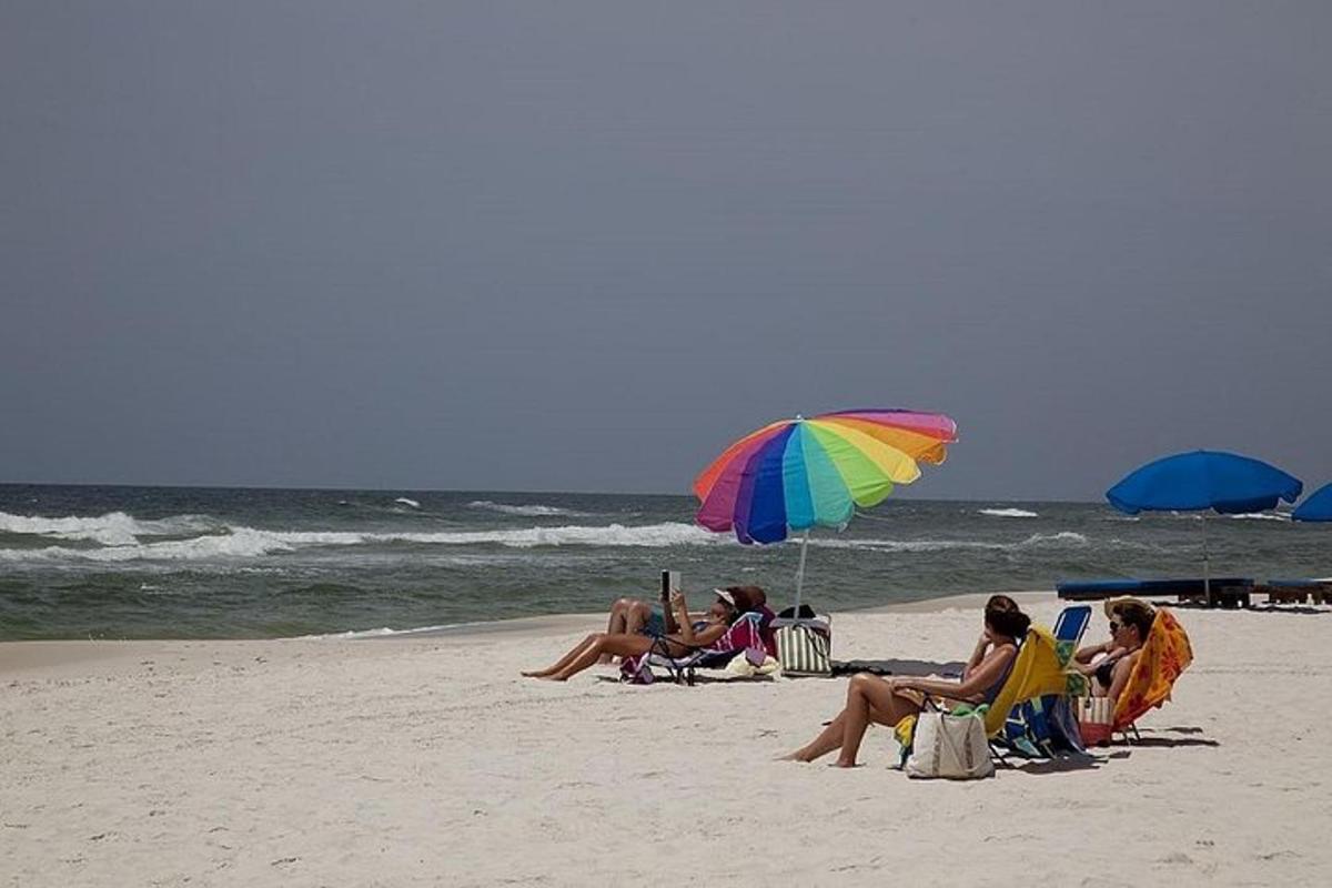 sekumpulan orang duduk di pantai di bawah payung
