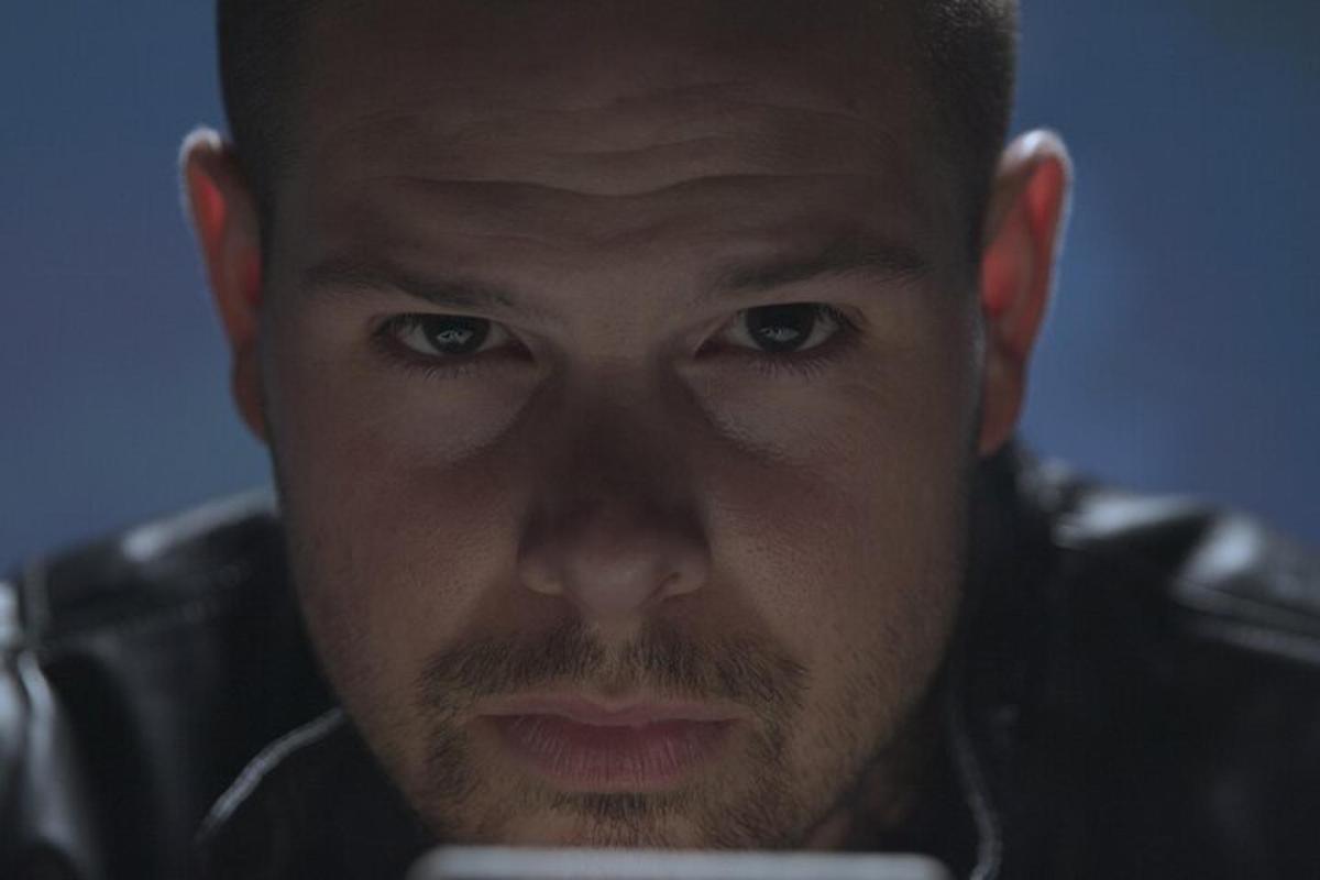 muž se dívá do kamery a drží v ruce mobilní telefon