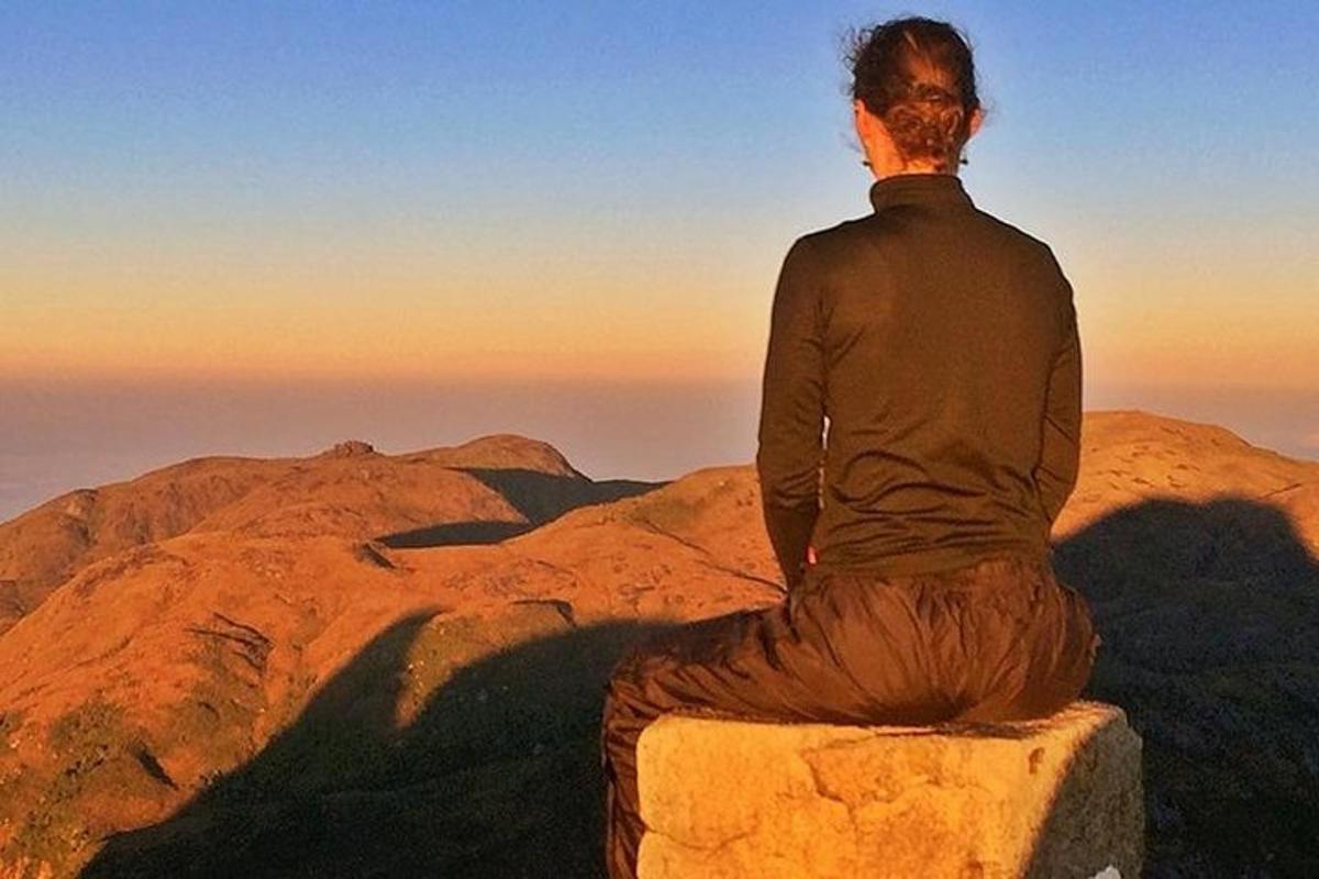moški sedi na skali in opazuje sončni zahod