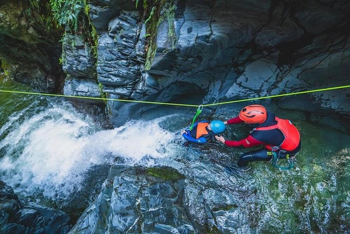 seseorang dengan rompi pelampung tergantung di tali di atas air terjun