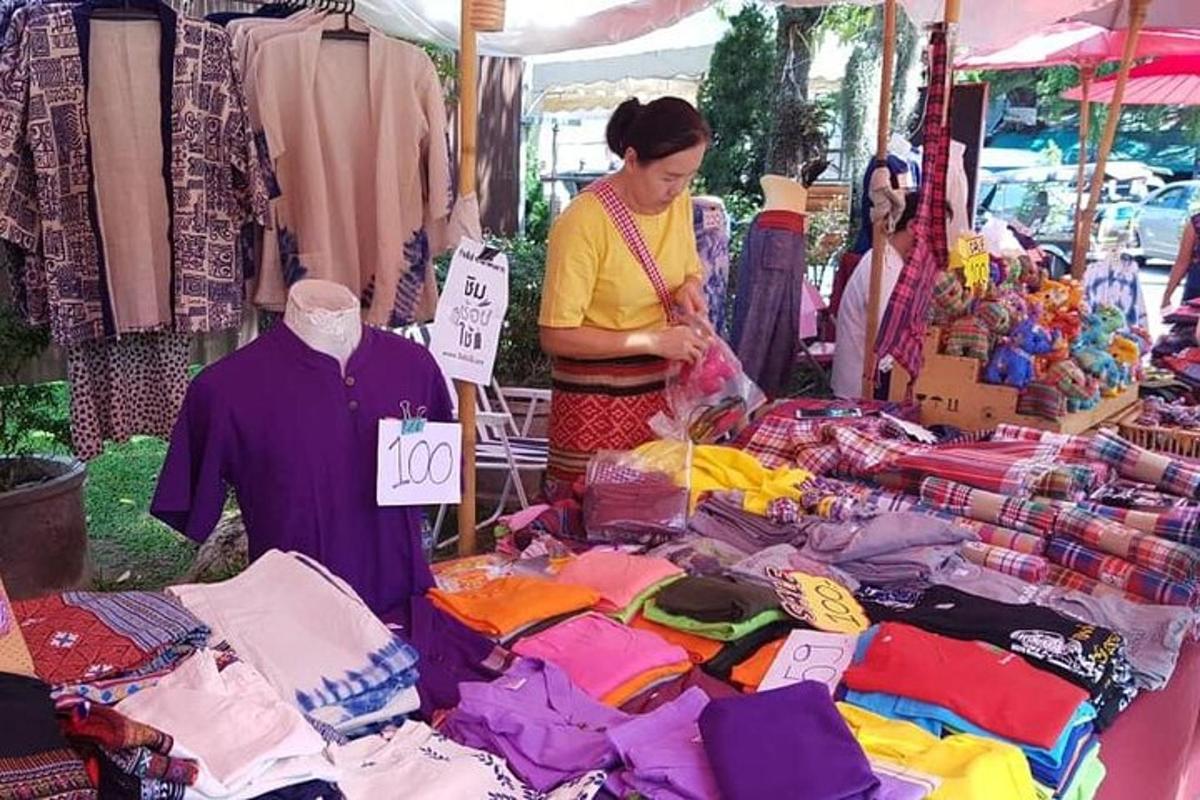 uma mulher parada em um mercado com uma pilha de roupas
