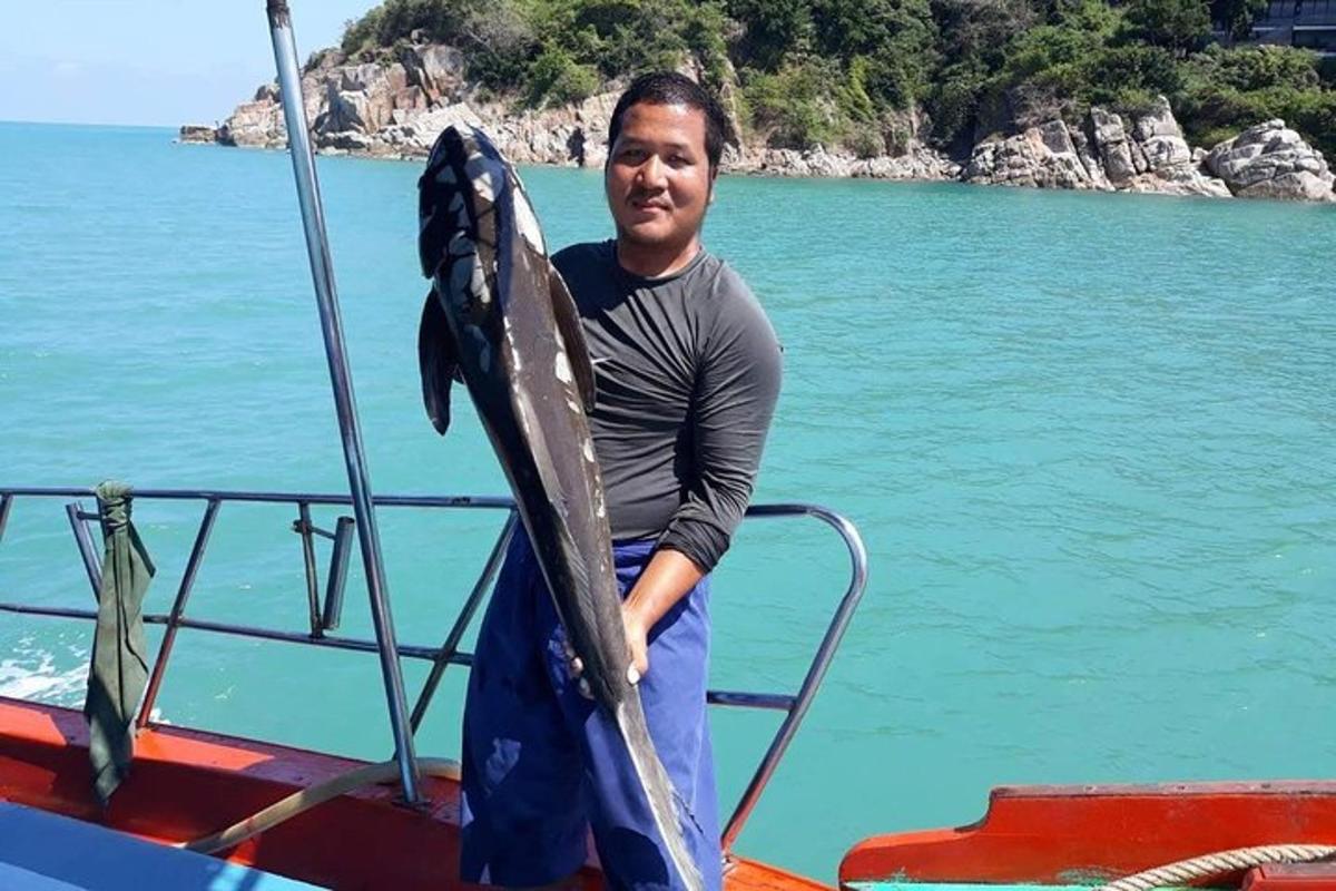 seorang pria berdiri di atas perahu sambil memegang ikan