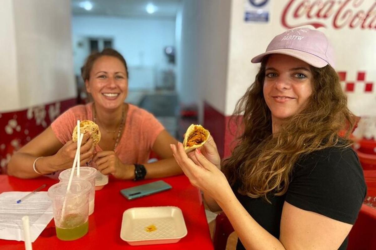 duas mulheres sentadas à mesa comendo cachorros-quentes