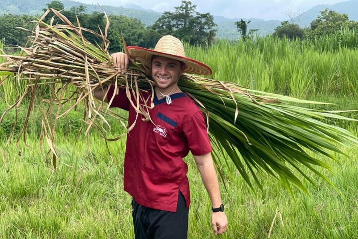 a man wearing a straw hat carrying a bunch of grass