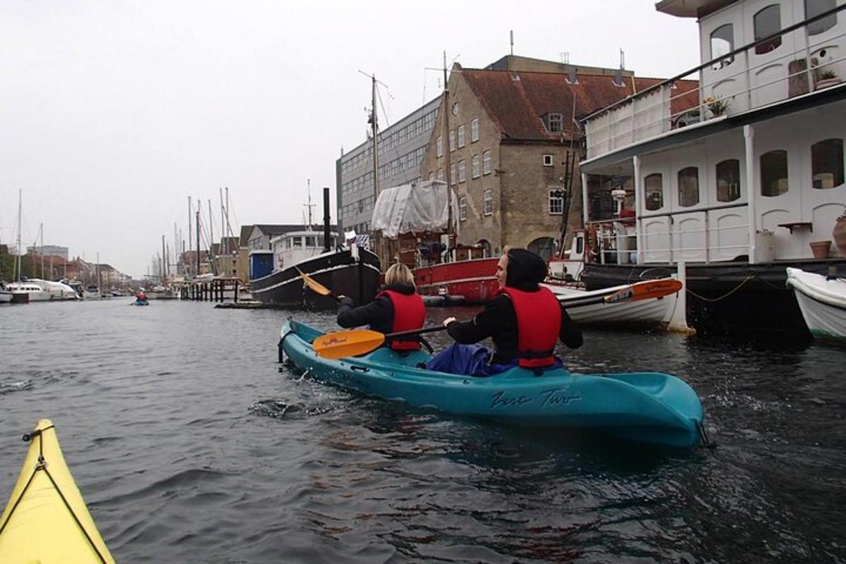 two people in a kayak in the water near boats