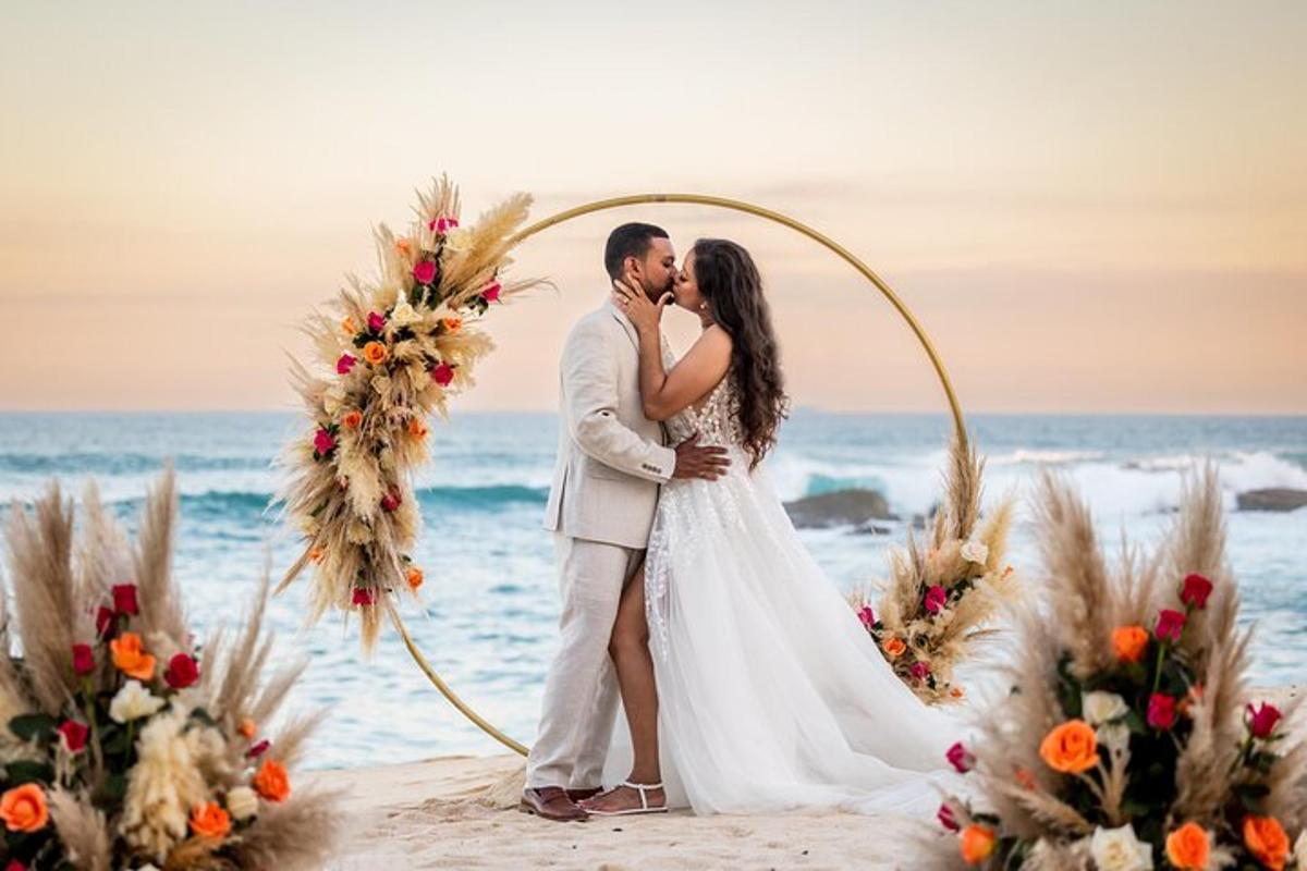 sepasang pengantin berciuman di bawah gapura pernikahan di pantai