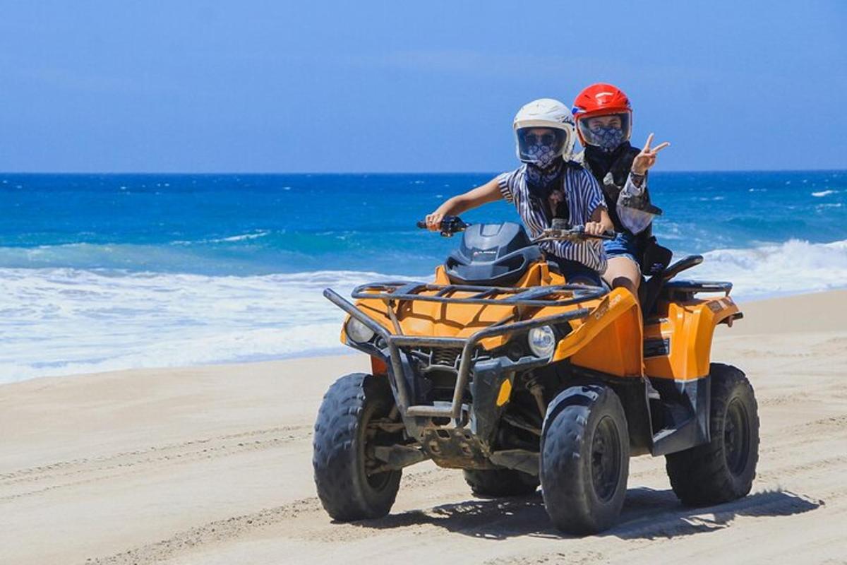 Dos personas viajando en un vehículo de cuatro ruedas en la playa