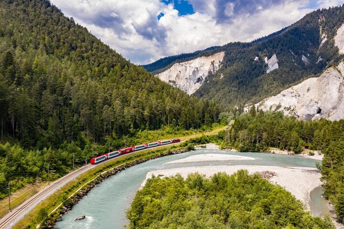 a train traveling along a river next to a mountain
