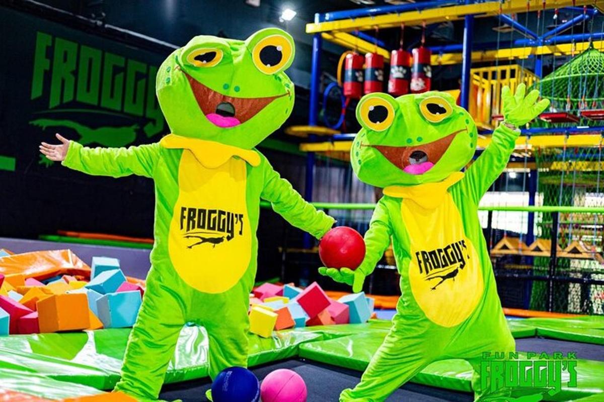 dva lidé v žabích kostýmech se drží za ruce na trampolíně