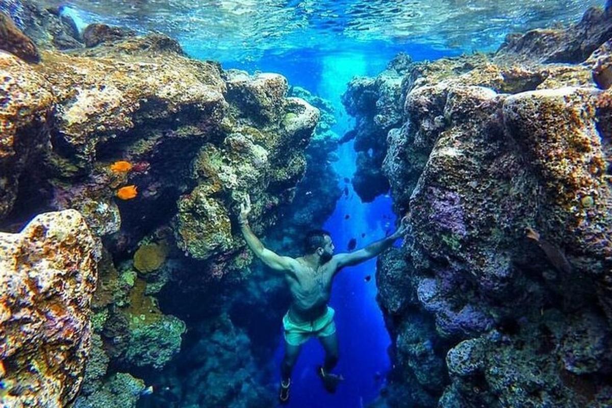 un homme debout dans l'eau à côté d'un récif