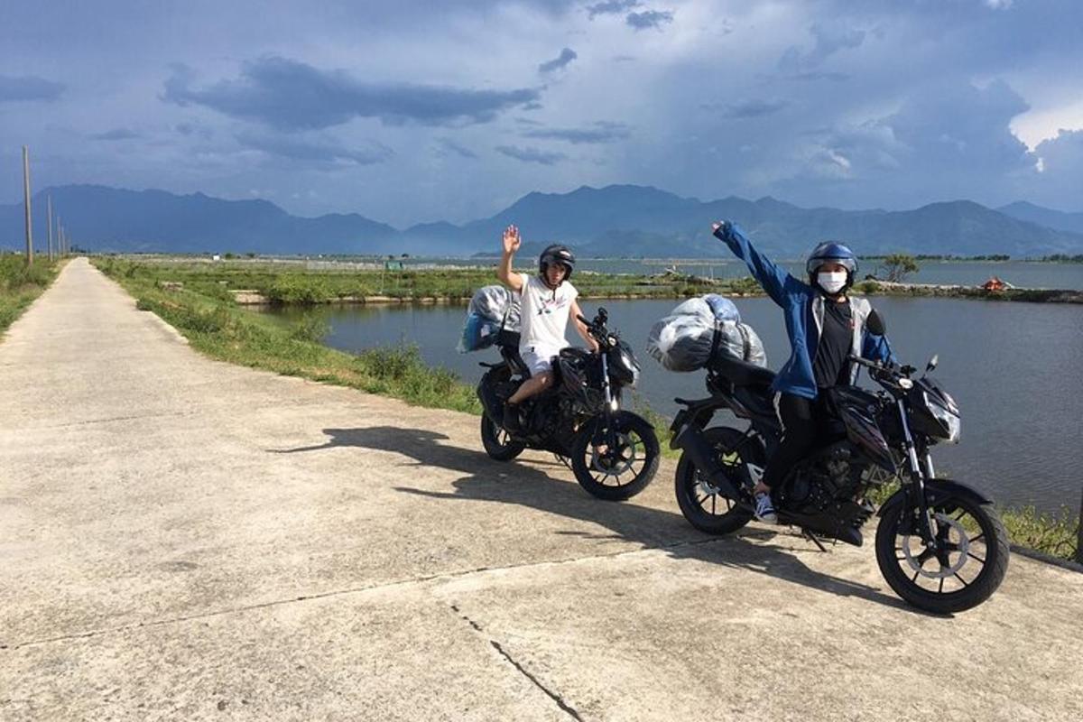 Dos personas que viajaban en motocicleta por una carretera cerca de un cuerpo de agua.